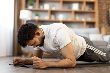 Arabian male athlete in activewear doing plank exercise on yoga mat during morning workout at home. Domestic training during free time. Concept of people, vitality and power.の写真素材