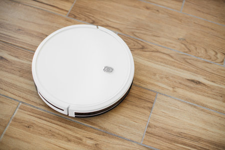 Top view of well-rounded wireless robotic vacuum cleaner dealing with dirt and dust on laminated floor inside apartment. Smart home device promoting comfortable lifestyle by making housework easier.の写真素材