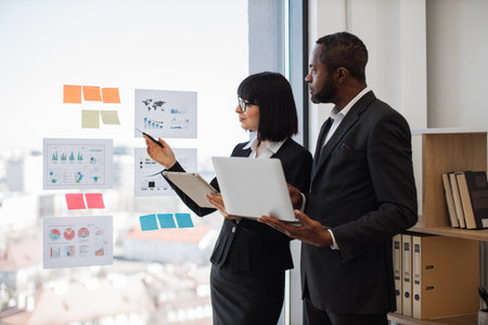 Young caucasian businesswoman with tablet in hand pointing at bar graphs while multicultural...