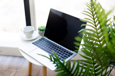 Wireless laptop placed on coffee table near white ceramic cup at bright office. Cozy and modern...
