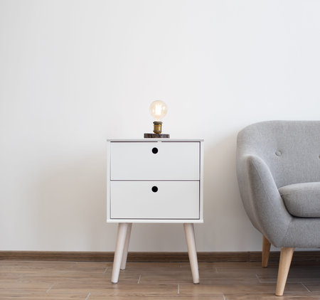 Industrial edison lamp on white contemporary bedside table near grey sofa in spacious studio room....