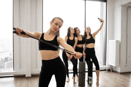 Beautiful young blonde in yoga clothes stretching skipping rope while fellow companions making...