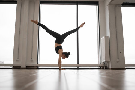 Young woman training alone at fitness studio with amazing city view throught panoramic window....