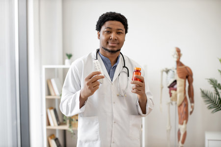 Portrait of african american male physician with stethoscope holding medicine containers while having break from consulting patients of surgery. Health professional in white coat choosing preparation.の写真素材