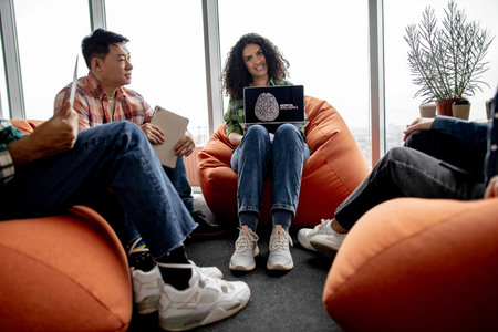 Smiling african american woman holding computer with AI image on screen while multiracial coworkers...