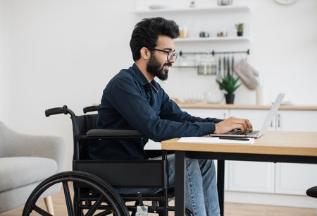 Close up view of smiling wheelchair user typing on portable computer while staying in distant workplace. Cheerful professional performing business project while doing full-time job from home.の写真素材