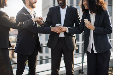 Crop of stylish corporate partners in trendy business suits shaking hands and agreeing about further cooperation. Multiethnic specialists feeling content and thanking each other for efficient meeting.の写真素材