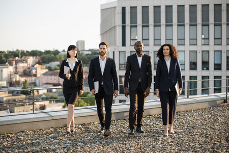 Team of business investors of different ethnicities dressed in suits walking proudly after making successful agreement. Male and female professionals feeling content and leaving office rooftop.の写真素材