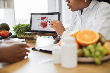 Cropped view of multiracial woman in white coat using tablet with picture of gastrointestinal tract...