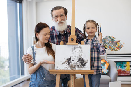 Artists family embracing together near easel with picture at bright art gallery. Grandfather with...