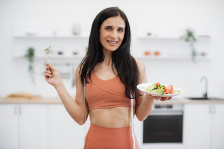 Energetic fitness woman enjoying smell of fresh cucumber while eating low-calorie food after efficient training at home. Active lady taking care of health by consuming organic meal and working out.の写真素材
