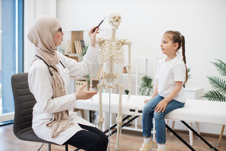 Doctor pointing at skull near girl on exam couch in clinicの写真素材