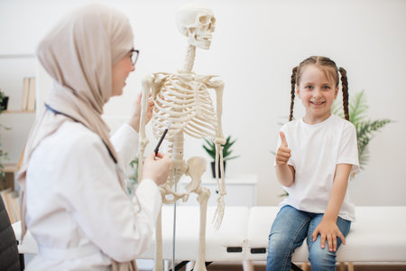 Family doctor illustrating bones to girl via skeleton modelの写真素材