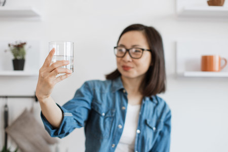 Half-empty glass of water held by chinese woman indoorsの写真素材