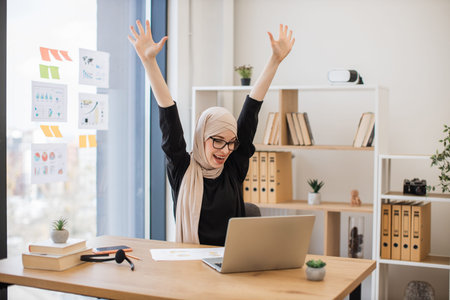 Muslim lady celebrating win with enthusiasm in workplaceの写真素材