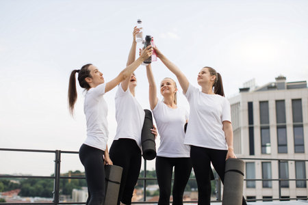 Female friends holding water bottles above heads outdoorsの写真素材