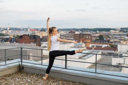 Person stretching leg muscles on roof handrails at sunsetの写真素材