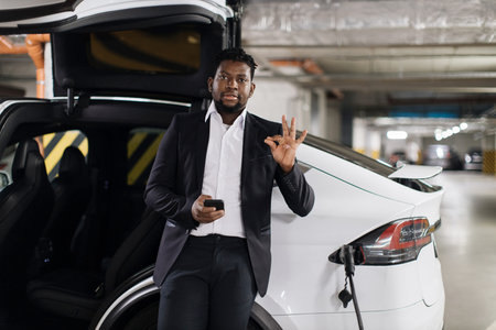 Male with phone posing near e-car being charged in parking