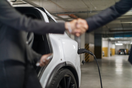 Charging cable plugged in e-car port near workers in parking