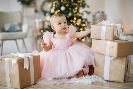 Cute little girl in pink dress sitting among Christmas giftsの写真素材