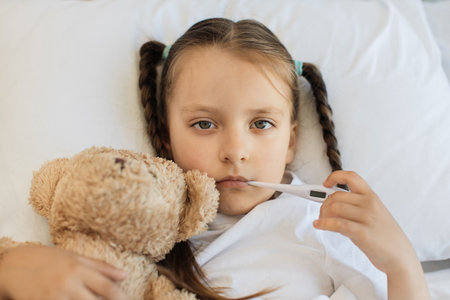 Sick girl lying on bed with digital thermometer in mouthの写真素材