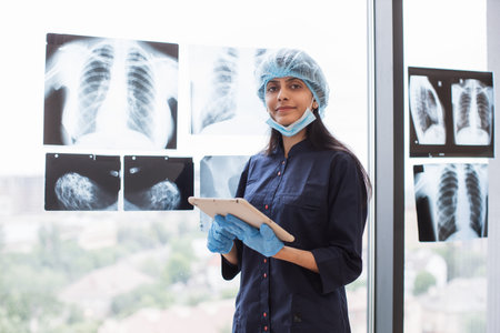 Hindu surgeon with tablet standing near glass with xray scan