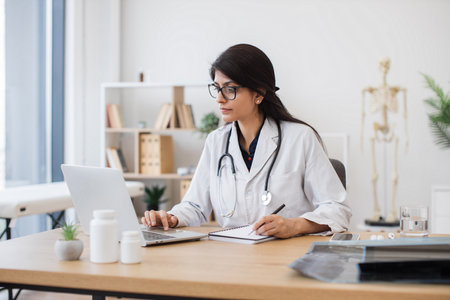 Female doctor with laptop writing prescription at officeの写真素材