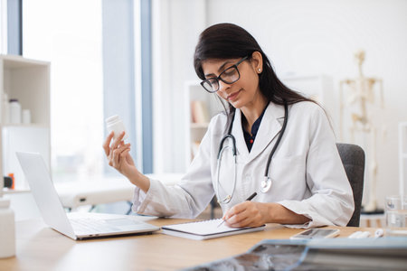 General practitioner with laptop examining pills in clinicの写真素材