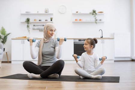 Muslim woman and little girl lifting dumbbells while looking at each other.の写真素材