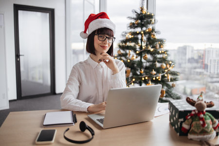Businesswoman sitting in office near xmas tree working on laptopの写真素材
