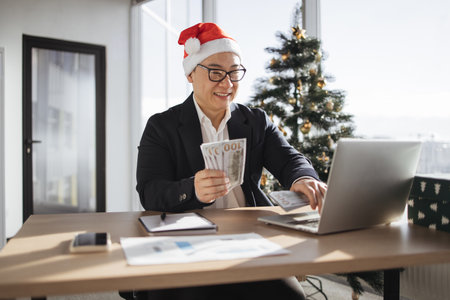 asian male accountant in Santa hat holding cash banknotes.の写真素材