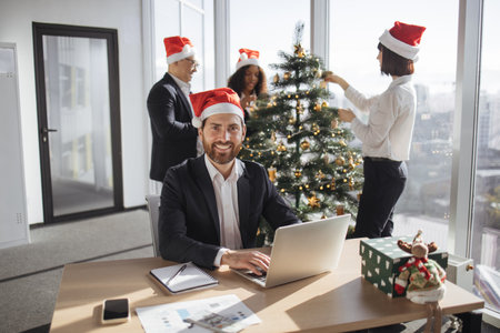 Businessman employee in santa hat sitting at desk using laptop looking camerの写真素材
