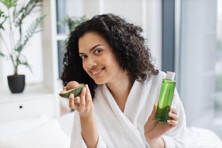 Female holding avocado and cosmetic oil bottle in bedroom