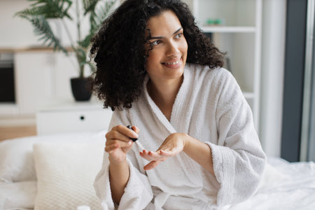Portrait of female in white bathrobe making manicureの写真素材