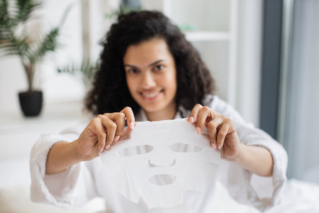 Focus on hands of relaxed female in after-shower outfit using tissue face maskの写真素材