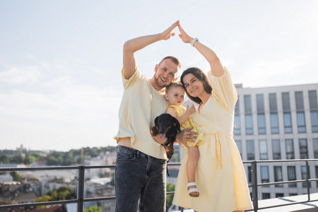 Family with raised up hands in form of house on city rooftopの写真素材