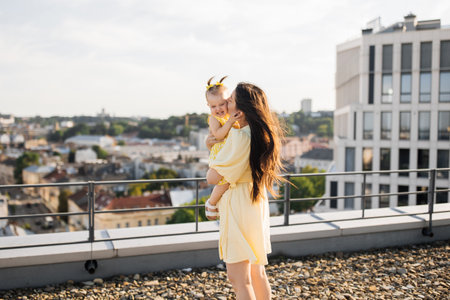 Happy mother holding and kissing daughter on rooftopの写真素材