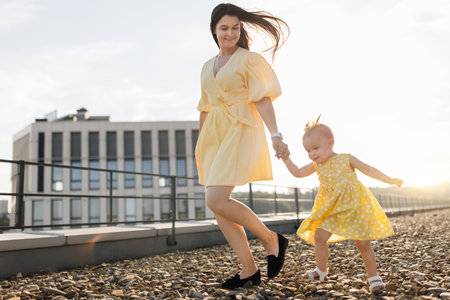 Smiling woman holding baby hand while walking on roofの写真素材