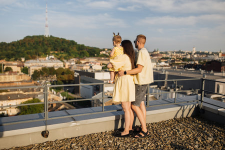 Caring husband hugging wife with child from behind on roofの写真素材