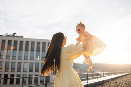 Adult lady holding and spinning with kid on city roofの写真素材