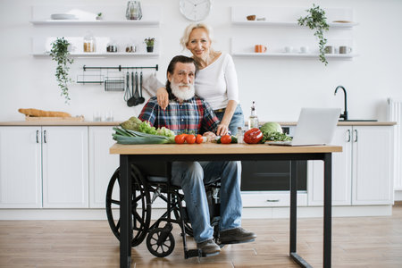 Disabled man with gray beard and wife preparing healthy vegetable salad.の写真素材