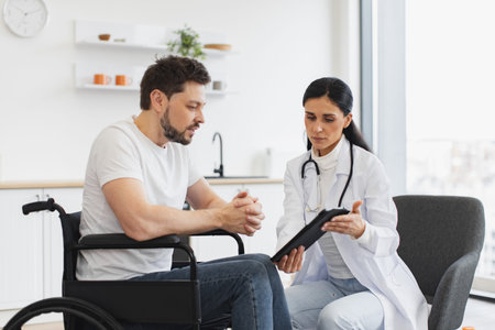Nurse talking to mature man on wheelchair, showing examination results.の写真素材