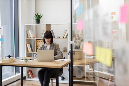Woman sitting with laptop at desk at modern company boardroom.