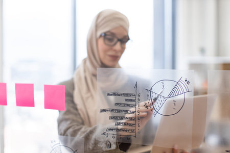 Arabian woman in hijab holding digital laptop and looking on financial graphic.の写真素材