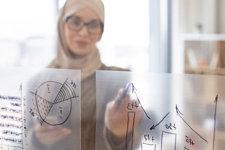 Muslim woman holding smartphone and looking on financial graphic.
