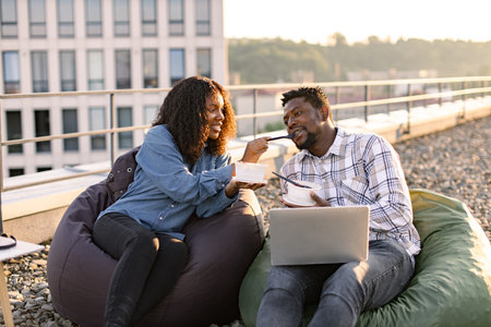 African couple eating healthy salad while sitting on beanbag chairs.の写真素材