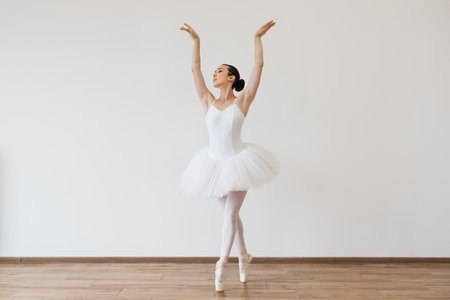 Caucasian woman ballerina in white tutu, dancing on pointe with arms overhead.の写真素材