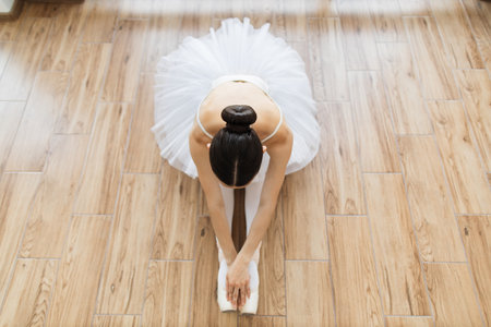 Portrait of young woman ballerina sitting on the wooden floor in dance club.の写真素材