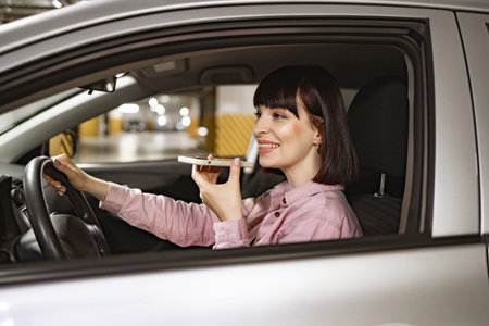 Female records audio messages using phone inside vehicle on underground parking.