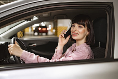 Woman in casual clothes sitting behind wheel of modern car, having phone call